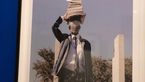 artwork depicting person in student uniform balancing books on head
